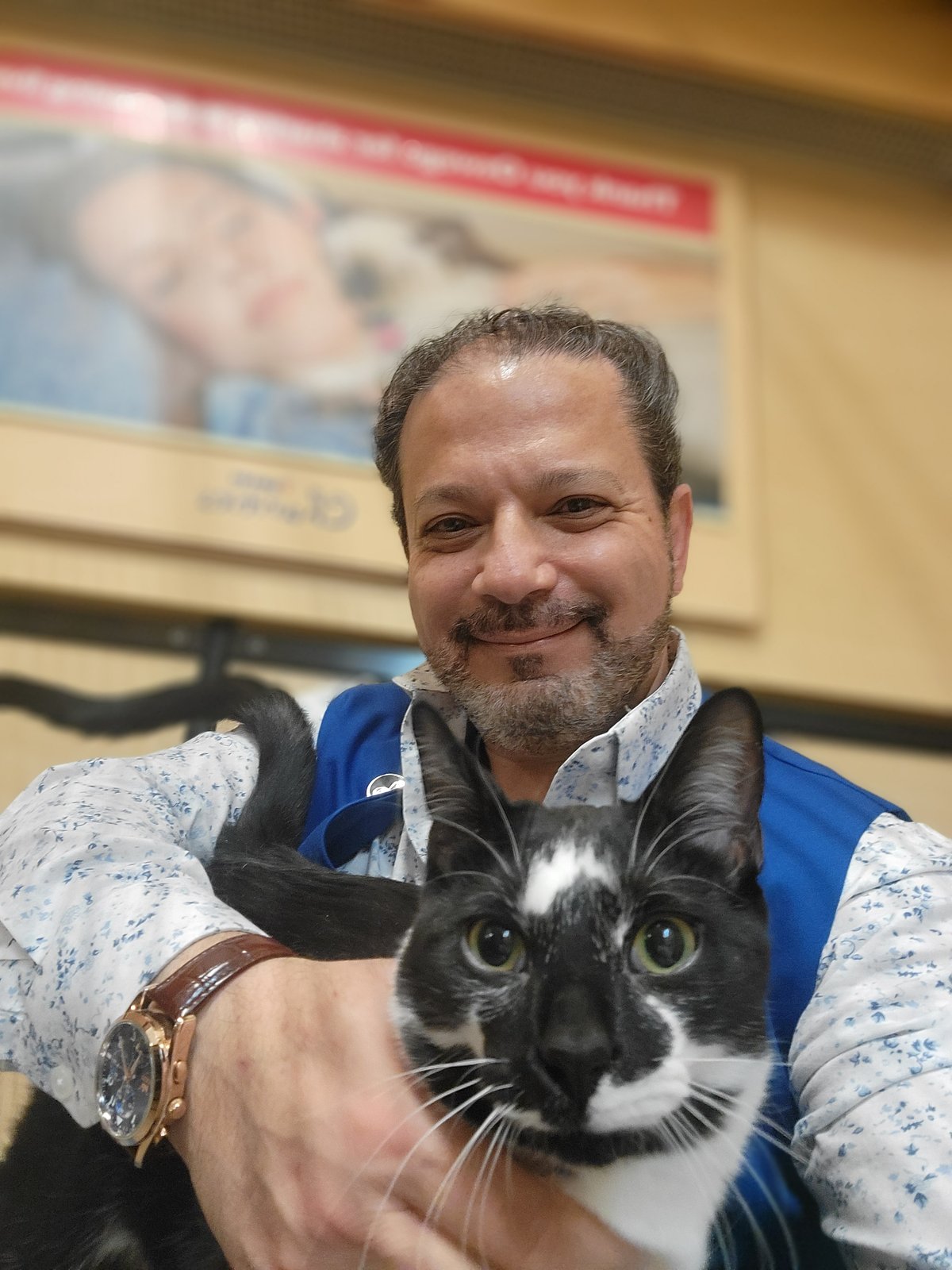 Dr. James in his blue volunteer vest holding a tuxedo cat at PetSmart Charities